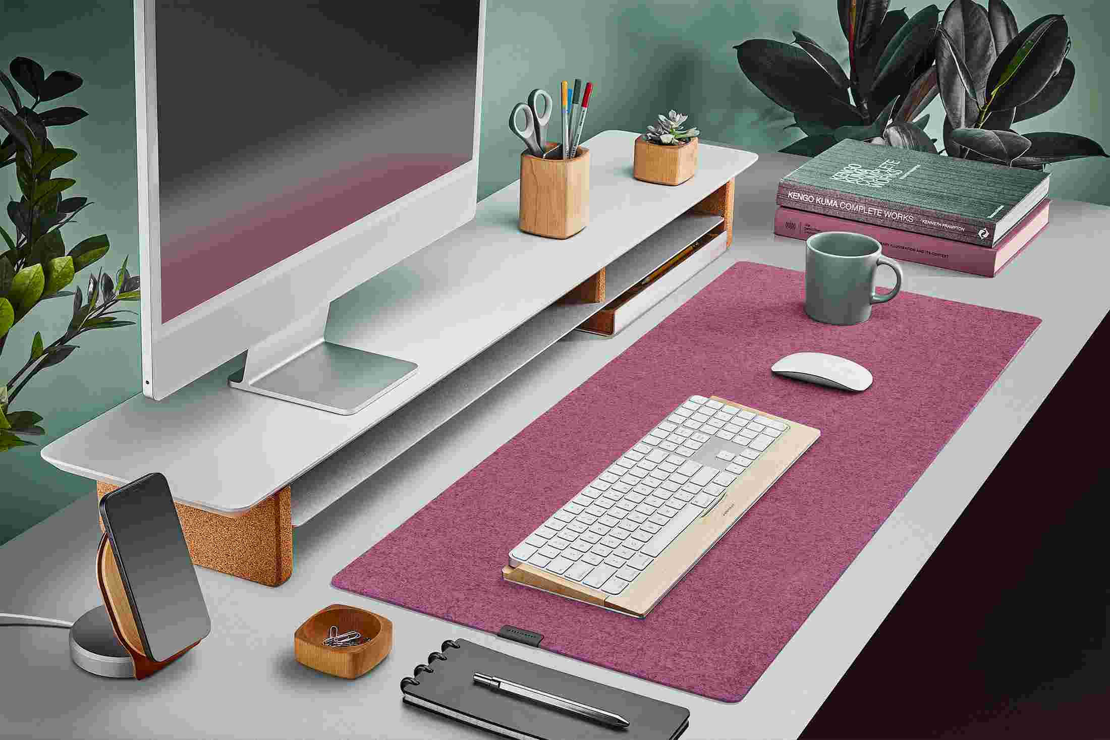 The Dark Pink Medium Plus Wool Felt Desk Pad runs the entire width of a standard desk, pictured here with matte white wood double-wide monitor stand.