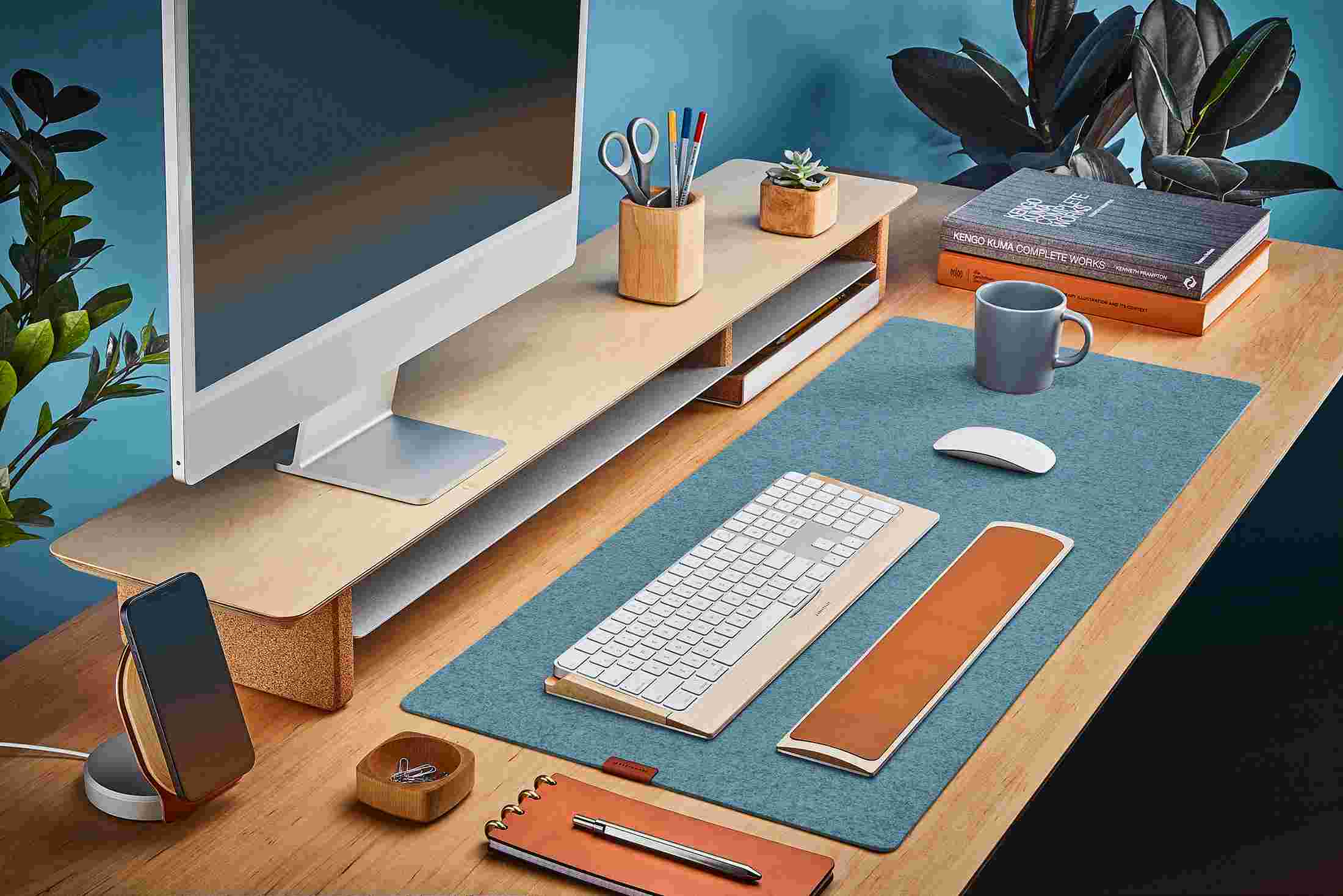 The Light Blue Medium Plus Wool Felt Desk Pad runs the entire width of a standard desk, pictured here with maple wood double-wide monitor stand.