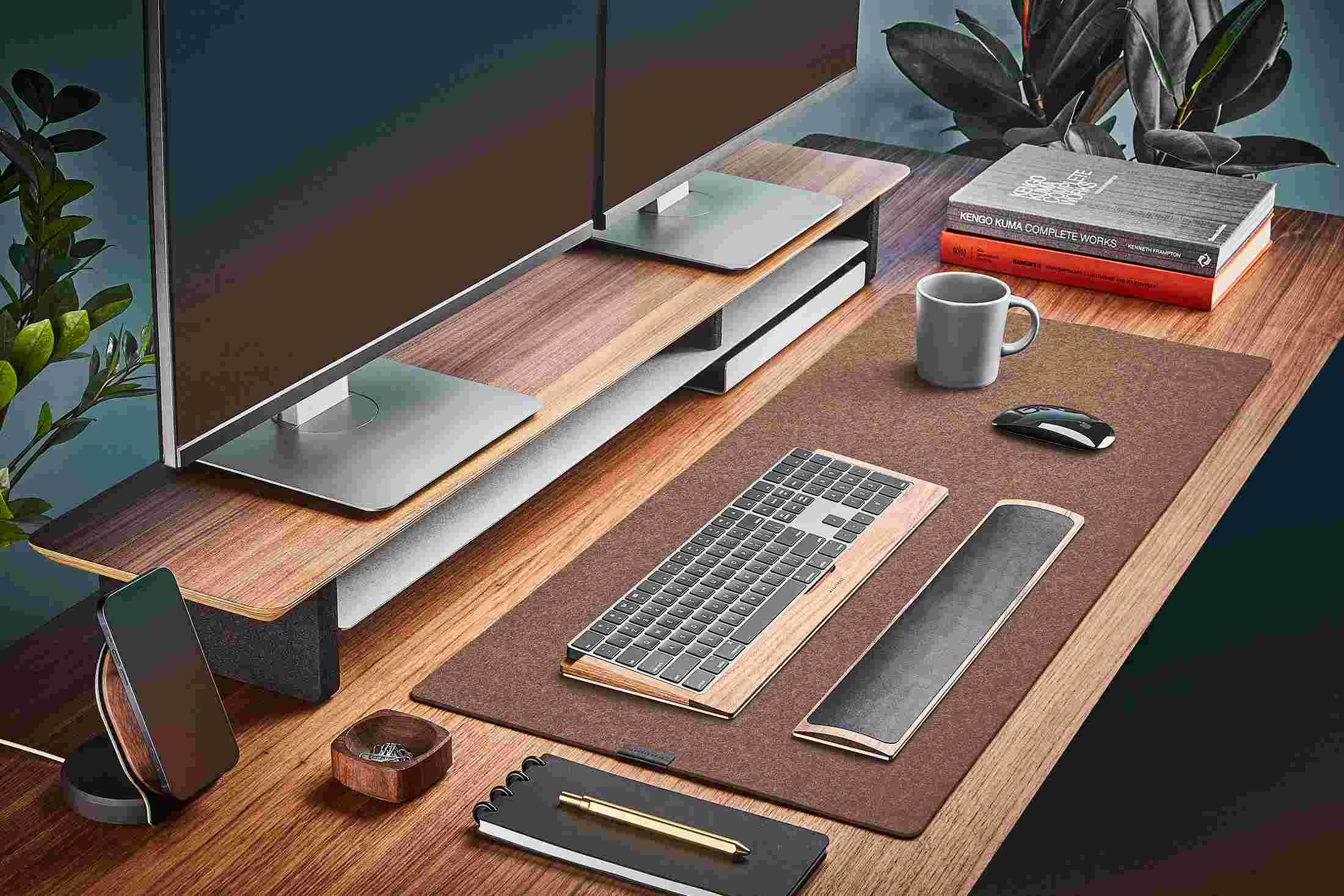 The Light Brown Medium Plus Wool Felt Desk Pad runs the entire width of a standard desk, pictured here with walnut wood double-wide monitor stand.