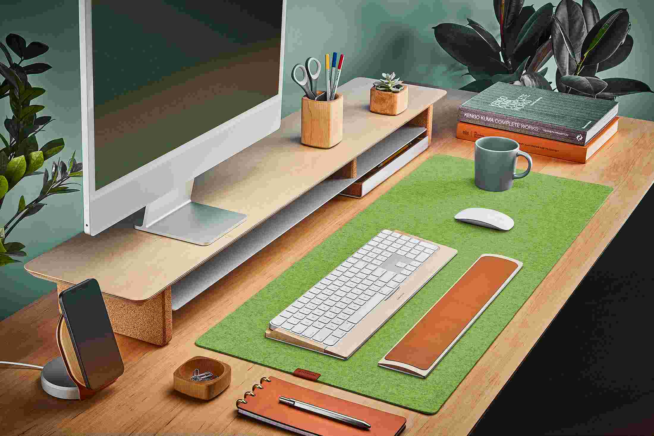 The Light Green Medium Plus Wool Felt Desk Pad runs the entire width of a standard desk, pictured here with maple wood double-wide monitor stand.