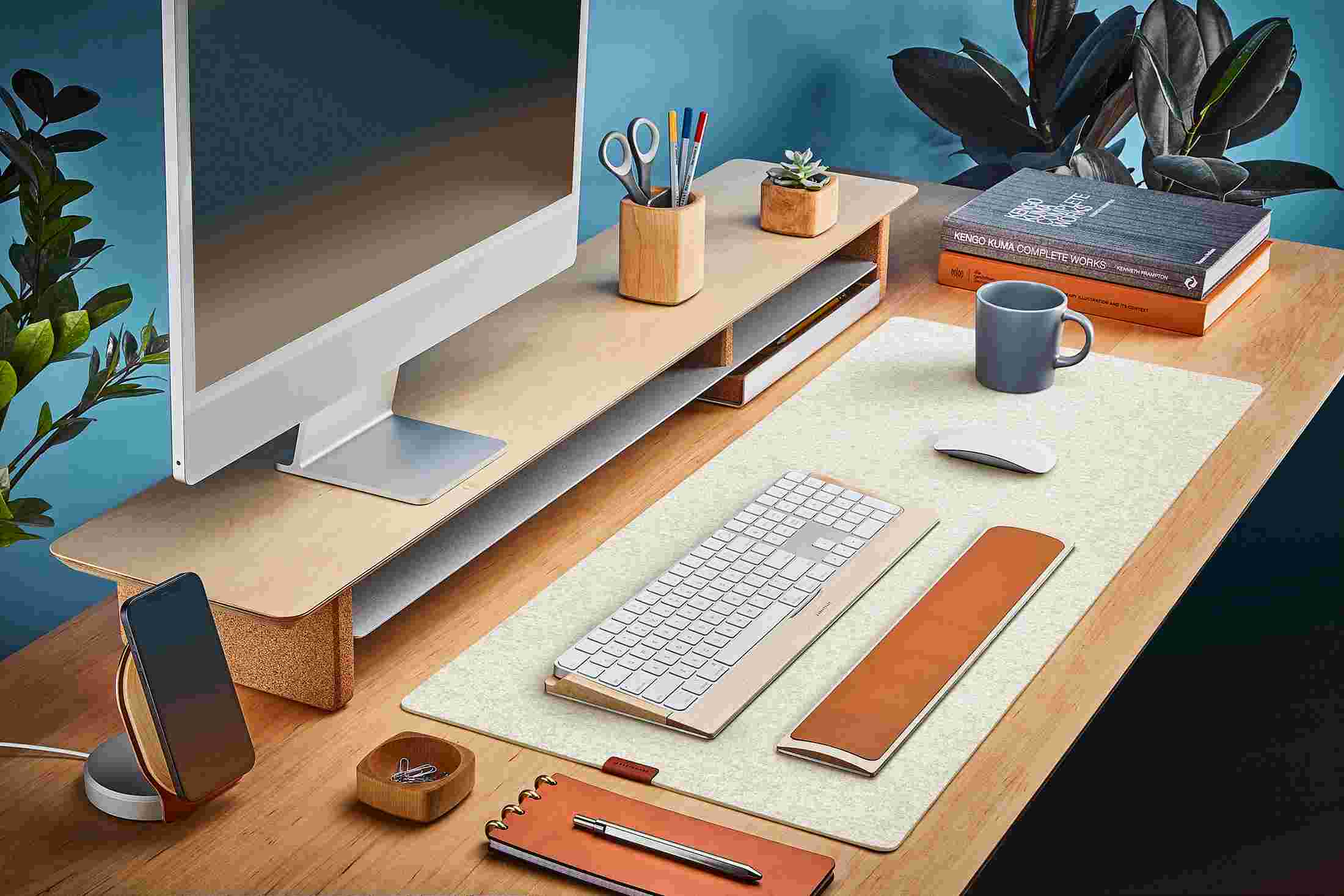 The White Medium Plus Wool Felt Desk Pad runs the entire width of a standard desk, pictured here with maple wood double-wide monitor stand.