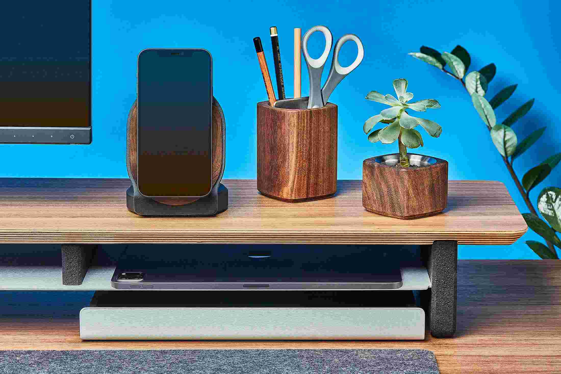 Walnut MagSafe Stand for iPhone 12 on wood monitor stand alongside walnut planters and premium leather desk mat.