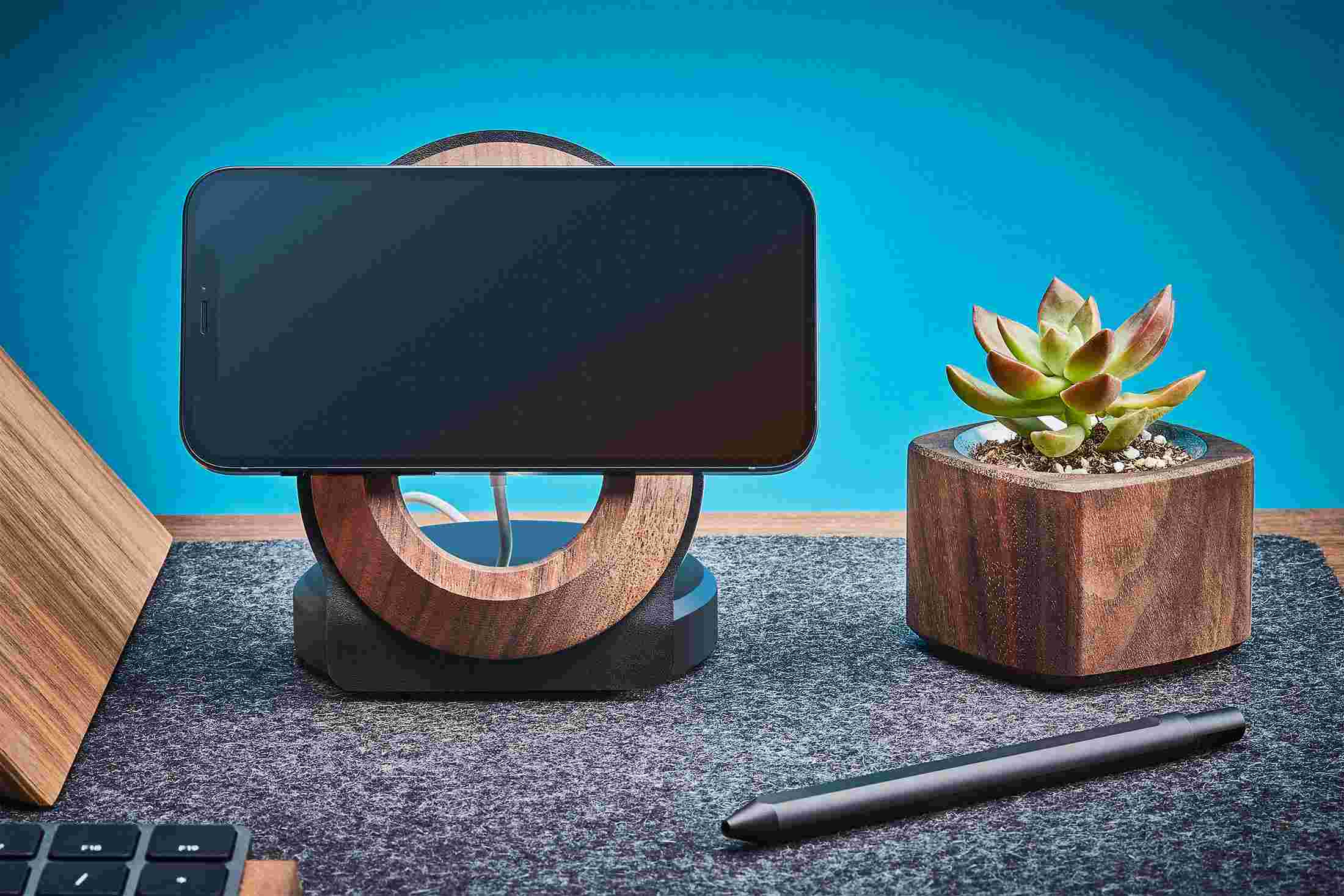 iPhone 12 suspended horizontally on vertical MagSafe charging stand made from walnut and black leather.