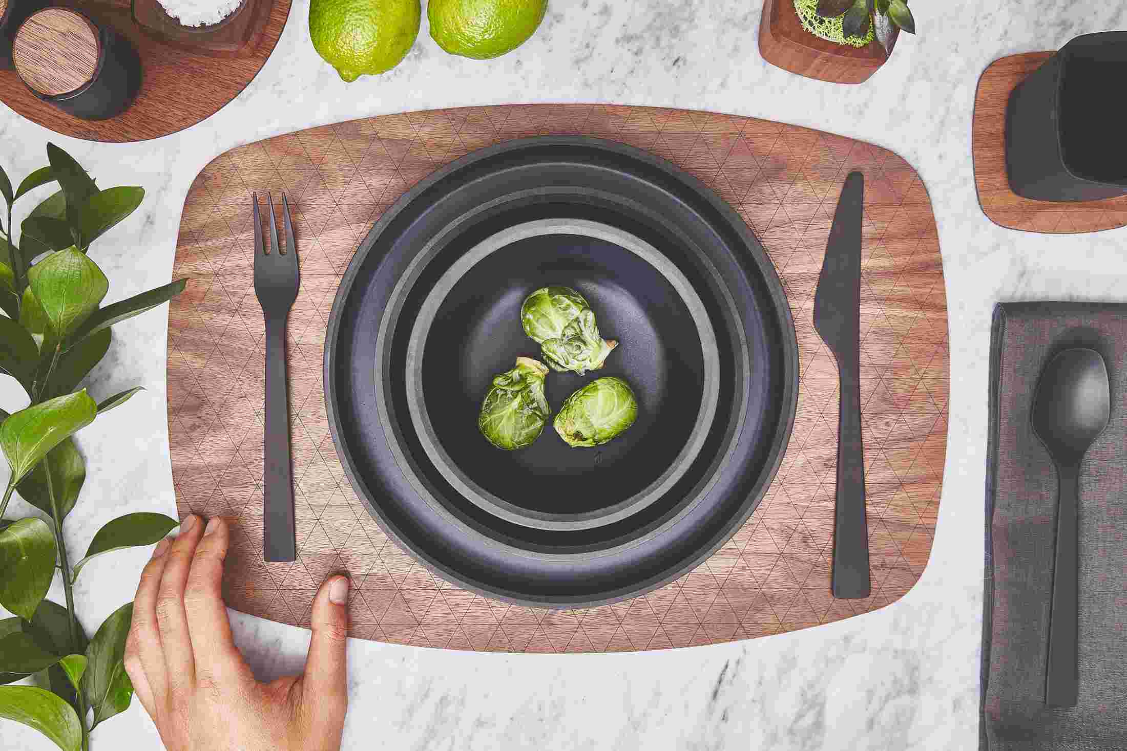 Overhead of the walnut tableware collection featuring black ceramic bowls, walnut placemat, and ceramic and wood salt & pepper shakers.